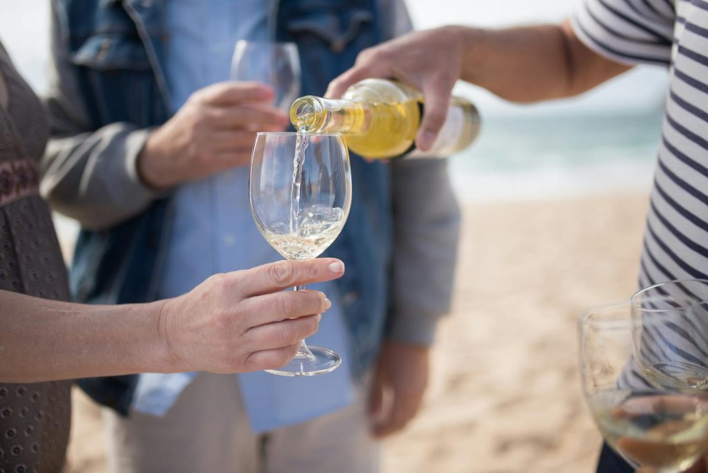 Handling And Serving Wine: The Dos And Donts A bottle of white wine being poured into glasses during a beach gathering in Long Island NY.